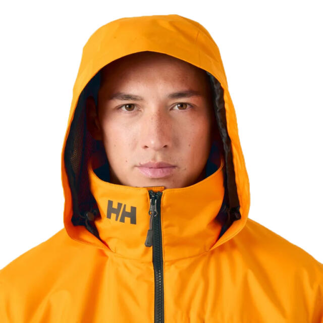 A close up of mans face with an orange Helly Hansen Waterproof Jacket with the hood up.